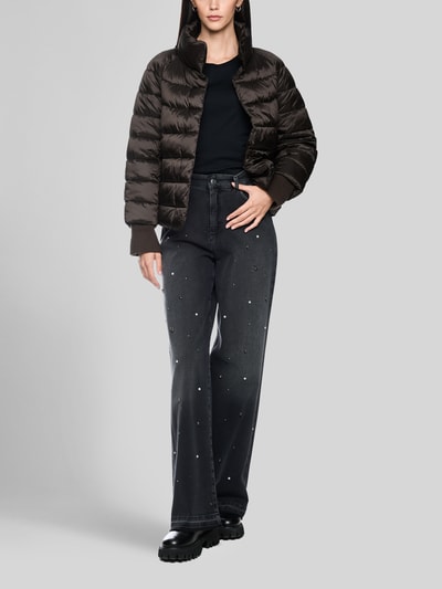 Frauenmodel trägt Steppjacke mit Stehkragen und Label-Detail von Marc Cain in Dunkelbraun, glänzende Textur, schwarze Hose, Ganzkörperansicht von vorne. Damen Steppjacke, Regular Fit, Eingrifftaschen, Rückenlänge 56 cm, Schulterbreite 41 cm, Brustweite 55 cm, Ärmellänge 73 cm.