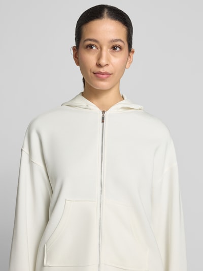 Kobiece model nosi Regular Fit Sweatjacke mit Kapuze Modell 'Marcella' von Christian Berg Woman, elastyczna mieszanka materiałów z domieszką modalu, kaptur, podzielona kieszeń kangurka, pas z tunelem, jasny kolor, gładka tekstura, zbliżenie na górną część ciała.