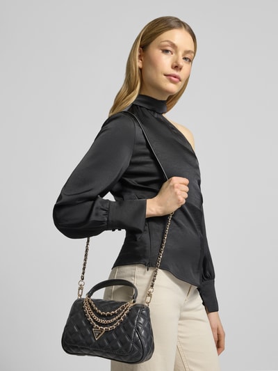 Frauenmodel trägt schwarze Handtasche mit Steppnähten Modell 'GIULLY II' von Guess, Label-Applikation, Tragehenkel, Magnetverschluss, Hauptfach, Überschlag, Schulterriemen, Detailaufnahme Oberkörper.