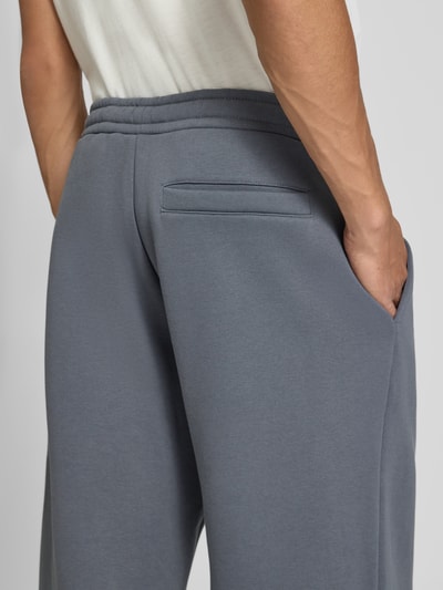 Männermodel trägt Sweatpants mit Logo-Print und Gesäßtasche von REVIEW, Baumwoll-Mix in Grau, Detailaufnahme Gesäßtasche, Nahaufnahme Rückansicht.