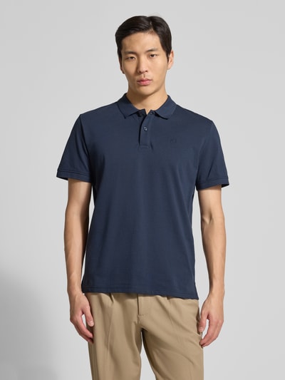Męski model nosi Regular Fit Poloshirt aus reiner Baumwolle von Tom Tailor, granatowa, jednolita, krój regular fit, logo, kołnierz polo, dekolt w szpic, krótka plisowana listwa, krótkie rękawy z ściągaczami, dół z rozcięciami po bokach, pikowana czysta bawełna, widok całej sylwetki z przodu.