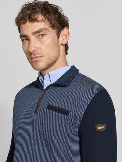 Männermodel trägt Sweatshirt mit Label-Details von bugatti in Blau mit Brusttasche, Troyer-Kragen, Nahaufnahme Oberkörper, elastischer Material-Mix mit Baumwoll-Anteil, gerader Schnitt, KI-modifiziertes Bild.