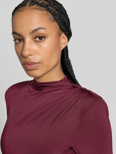 Frauenmodel trägt Slim Fit Minikleid aus Viskose-Mix von ROTATE in Bordeaux mit Stehkragen, Raffungen, langärmelig, Nahaufnahme Oberkörper.