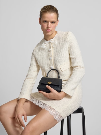Frauenmodel trägt Crossbody Bag in Stepp-Optik von Tory Burch in Schwarz, Ketten-Trageriemen, Logo-Detail, Nahaufnahme Oberkörper.