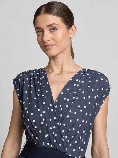 Vrouwenmodel draagt Regular Fit Jumpsuit mit V-Ausschnitt van Vera Mont in donkerblauw met witte stippen, elastische materiaalmix, getailleerd, mouwloos design, plooien, tailleband, nahaufnahme bovenlichaam. Context: dames jumpsuit, ruglengte maat 36: 39 cm, borstwijdte: 44 cm, mouwlengte: 18 cm, totale lengte: 160 cm, binnenbeenlengte: 93 cm.