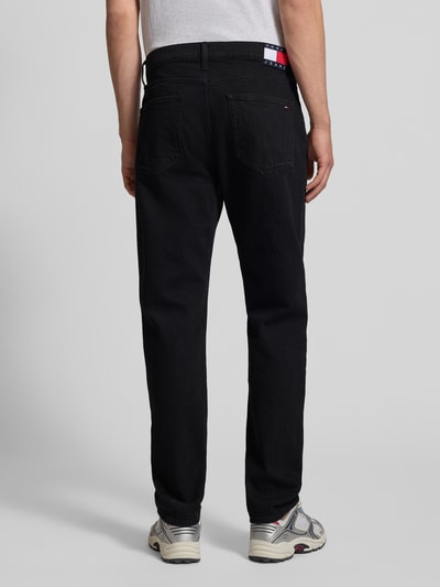 Männermodel trägt schwarze Straight Fit Jeans aus Baumwoll-Mix Modell 'RYAN' von Tommy Jeans, 5-Pocket-Design, Ganzkörperansicht Rückansicht.