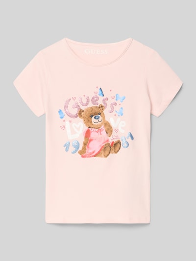Mädchen trägt Dziecięcy t-shirt z mieszanki bawełny i elastanu, krój regular fit, okrągły dekolt, detal z logo Guess, długość tyłu 44 cm przy rozmiarze 116, jasnoróżowy z nadrukiem misia, całkowity widok z przodu.