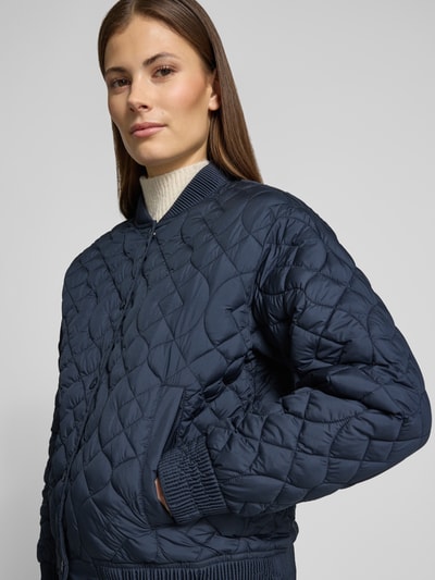 Modelka kobieca nosi Jacke mit Stehkragen und Eingrifftaschen od Fuchs Schmitt, krój regular fit, granatowa, pikowana faktura, z kieszeniami, widok z przodu, zbliżenie na górną część ciała, długość pleców w rozmiarze 36: 58 cm, szerokość ramion w rozmiarze 36: 48 cm, szerokość klatki piersiowej w rozmiarze 36: 57 cm, długość rękawa w rozmiarze 36: 56 cm.