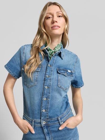 Frauenmodel trägt Flared Denim-Jumpsuit Modell 'KIMMY' von Mustang aus Baumwoll-Elasthan-Mix mit Umlegekragen, Knopfleiste, Brusttaschen und Label-Detail, Denim-Optik, Nahaufnahme Oberkörper. Rückenlänge 53 cm, Brustweite 46 cm, Ärmellänge 20 cm, Gesamtlänge 165 cm, Innenbeinlänge 83 cm bei Größe S.