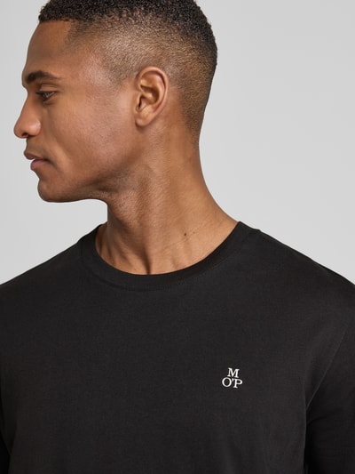 Männermodel trägt T-Shirt mit Label-Print von MARC O’POLO, schwarze Baumwolle, gerippter Rundhalsausschnitt, Nahaufnahme Oberkörper.