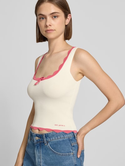 Frauenmodel trägt Crop Top aus Viskose-Mix mit Wellensaum Modell 'Anele' von OH APRIL, elfenbeinfarben mit rosa Detail, Nahaufnahme Oberkörper. Gerippte Textur, Schnürung vorn, Stricktop, Rückenlänge S: 27 cm.