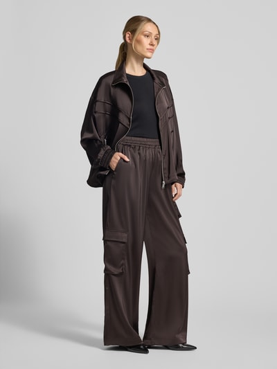 Frauenmodel trägt Loose Fit Stoffhose mit elastischem Bund Modell 'darzi' von Gestuz, Material-Mix mit Stretch-Anteil in Braun, Cargotaschen, Ganzkörperansicht von vorne.
