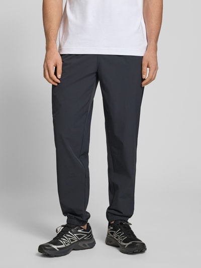 Männermodel trägt Trackpants mit Reißverschlusstaschen Modell 'HALO MOVE' von HALO, Material-Mix mit Stretch-Anteil, Regular-Fit, Label-Print, dunkle Farbe, glatte Textur, Herren, Innenbeinlänge bei Größe M 78 cm, Ganzkörperansicht von vorne.