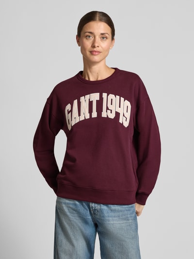 Frauenmodel trägt Relaxed Fit Sweatshirt aus reiner Baumwolle von GANT in Dunkelrot mit cremefarbenem Aufdruck, Jeans, Nahaufnahme Oberkörper. Damen Sweatshirt von GANT.