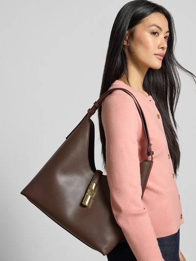 Frauenmodel trägt Handtasche aus echtem Leder Modell 'GOCCIA' von FURLA in Dunkelbraun mit Goldverschluss, glatte Textur, Nahaufnahme Oberkörper. Hauptfach mit Magnetverschluss, verstellbarer Schulterriemen, Innenfach mit Reißverschluss, Maße: 24x31x17 cm, Riemenlänge 42 cm.