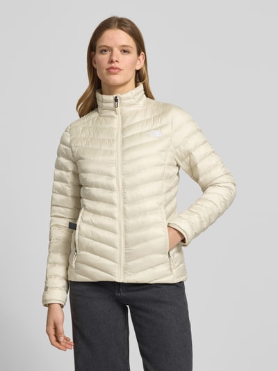 Kobiece model prezentuje Steppjacke mit Stehkragen und Label-Stitching von The North Face, jasny beż, pikowanie, krój regular fit, stójka, wyhaftowane logo, zamek błyskawiczny, kieszenie zapinane na zamek błyskawiczny, długość tyłu w rozmiarze S: 62 cm, szerokość ramion w rozmiarze S: 38 cm, szerokość w rozmiarze S: 46 cm, długość rękawów w rozmiarze S: 64 cm, całe ciało, widok z przodu