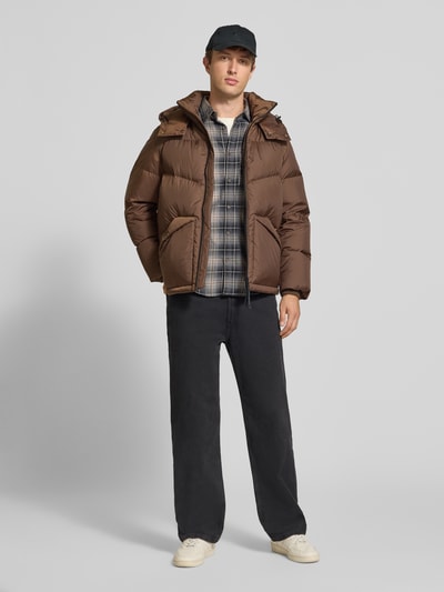Männermodel trägt Regular Fit Daunenjacke mit Kapuzenkragen von Marc O'Polo in Braun, kombiniert mit kariertem Hemd, Ganzkörperansicht von vorne, Herren Steppjacke von Marc O'Polo DENIM.