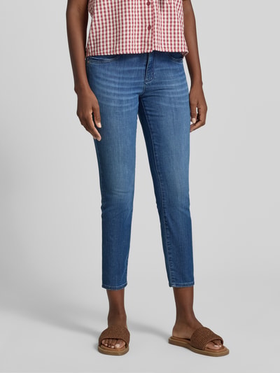 Frauenmodel trägt Slim Fit Jeans aus Baumwoll-Mix Modell 'SHAKIRA' von Brax in Denim-Optik mit Label-Patch, Mid Waist, Gürtelschlaufen, Knopf und verdecktem Reißverschluss, Ganzkörperansicht von vorne.