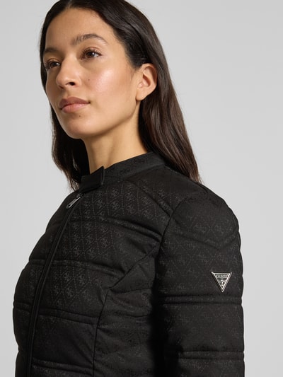 Kobiece model nosi kurtkę pikowaną z logo-muster model 'NEW VONA' od Guess z czarnej mieszanki materiałów z dodatkiem streczu, slim fit, stójka i kieszenie na zamek błyskawiczny, widok z przodu zbliżenie na górną część.