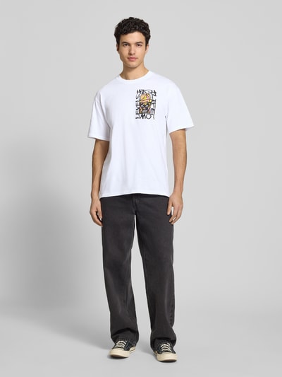 Męski model nosi męski t-shirt z nadrukiem, model 'HATTY MAN' od Edwin, bawełna, krój relaxed fit, okrągły dekolt, długość tyłu w rozmiarze M: 73 cm, widok całej sylwetki z przodu.