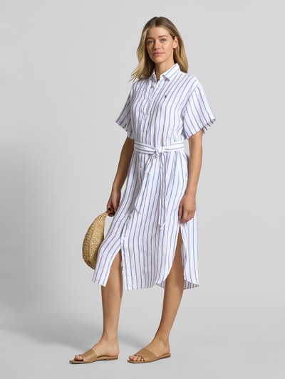 Modelka kobieca nosi Oversized Hemdblusenkleid aus reinem Leinen od Lauren Ralph Lauren, białe z niebieskimi paskami, midi, krój oversize, materiał lniany, krótki rękaw, widok całej sylwetki z przodu.