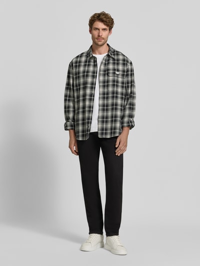 Männermodel trägt Tapered Fit Jeans aus Baumwoll-Mix Modell 'Redford' von Wrangler, dunkles Design, glatte Struktur, Ganzkörperansicht von vorne. Herren Tapered Fit Jeans von Wrangler.