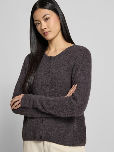 Frauenmodel trägt Strickjacke aus Alpaka-Mix von MOS MOSH in dunklem Braun mit geripptem Rundhalsausschnitt und Knopfleiste, lockere Passform, Nahaufnahme Oberkörper.