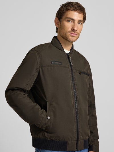 Männermodel trägt Blouson mit Stehkragen und Eingrifftaschen von camel active, Reißverschluss, Label-Detail, Nahaufnahme Oberkörper.