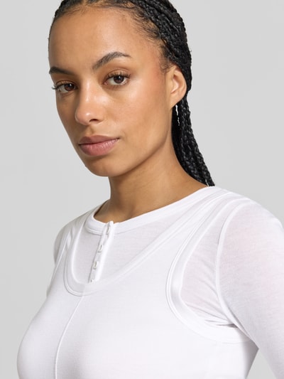 Frauenmodel trägt Longsleeve aus Viskose-Mix von BAUM & PFERDGARTEN in Weiß, eng anliegend, 2-in-1-Look, Nahaufnahme Oberkörper.