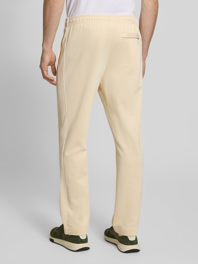 Männermodel trägt Regular Fit Sweatpants mit Baumwoll-Anteil von Lacoste in Beige, unifarben, Galonstreifen, Sweat-Material, Ganzkörperansicht Rückansicht.
