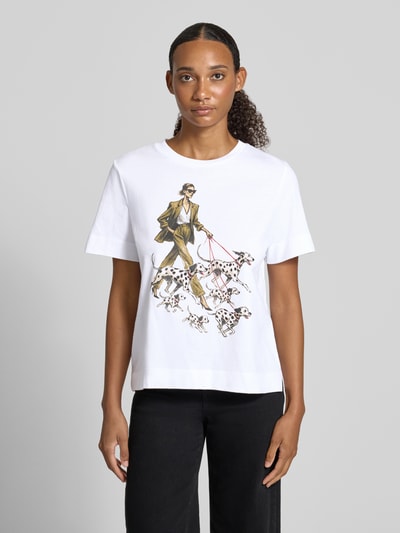 Modelka prezentuje Damski t-shirt z bawełny o kroju regular fit z nadrukiem z motywem i obszyciem z kamieni stras Regular Fit T-Shirt aus reiner Baumwolle von Rich & Royal, nadruk z motywem, obszycie z kamieni stras, długość tyłu w rozmiarze S: 57 cm, widok całej sylwetki z przodu.