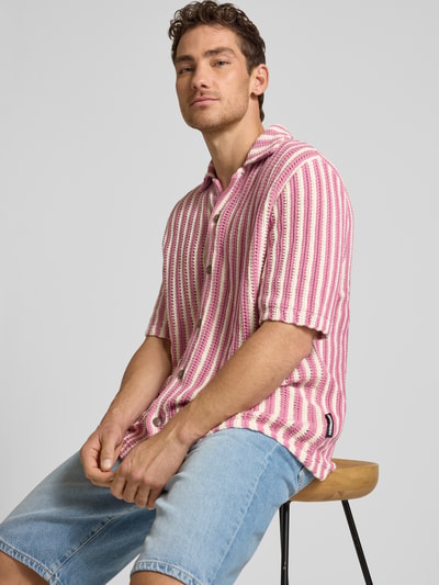 Männermodel trägt Relaxed Fit Poloshirt aus reiner Bio-Baumwolle von Armedangels mit gestreiftem Allover-Muster, Stricktextur, Nahaufnahme Oberkörper.