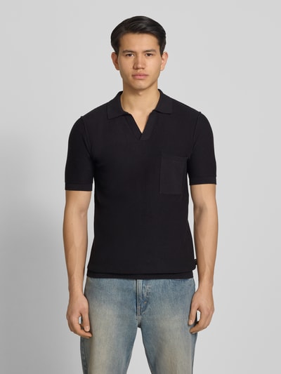 Männermodel trägt Slim Fit Poloshirt in Strick-Optik von Replay in Schwarz mit V-Ausschnitt und Brusttasche, Ganzkörperansicht von vorne.