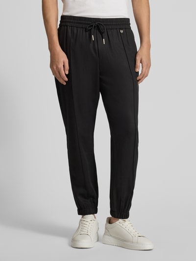 Männermodel trägt Loose Fit Stoffhose aus Lyocell-Leinen-Mix von Antony Morato, schwarze Farbe, elastischer Bund mit Tunnelzug, französische Eingrifftaschen, Gesäßtaschen, Ganzkörperansicht von vorne.