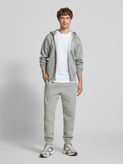 Männermodel trägt Sweatpants mit Label-Stitching und Gesäßtasche von Nike aus Baumwoll-Mix in Hellgrau, Regular-Fit, Ganzkörperansicht von vorne.