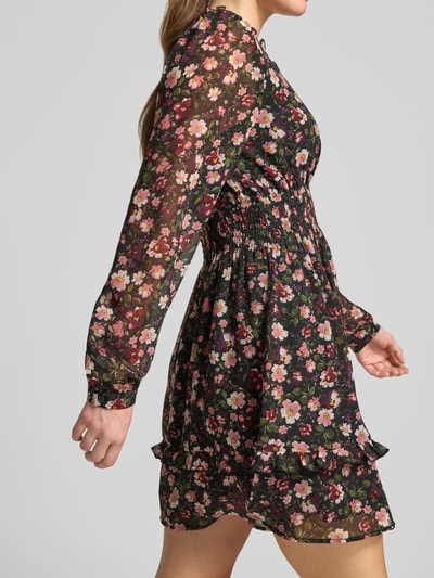 Frauenmodel trägt Minikleid im Allover-Look mit elastischem Taillenband von Apricot, schwarzer Stoff mit buntem Blumenmuster, A-Linie, Rüschen, V-Ausschnitt, Nahaufnahme Oberkörper seitlich.