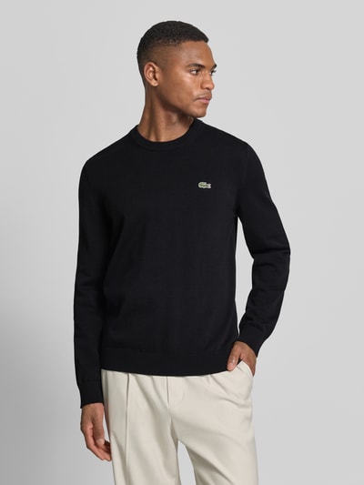 Männermodel trägt Regular Fit Strickpullover aus Baumwoll-Mix von Lacoste, Optik: Unifarben, Logo-Stitching, Ganzkörperansicht von vorne.