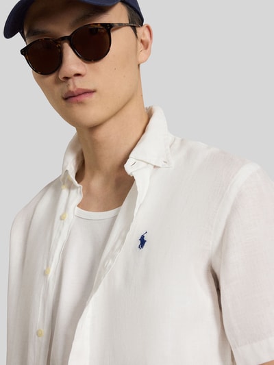 Mannelijk model draagt Regular Fit Leinenhemd mit Button-Down-Kragen van Polo Ralph Lauren, effen wit linnen, logo-stiksel, korte mouwen, doorlopende knoopsluiting, licht afgeronde zoom, close-up bovenlichaam.