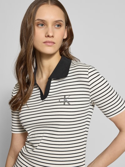 Frauenmodel trägt Slim Fit Poloshirt mit Label-Stitching von Calvin Klein Jeans in Schwarz-Weiß gestreift, Ripp-Optik, Nahaufnahme Oberkörper.
