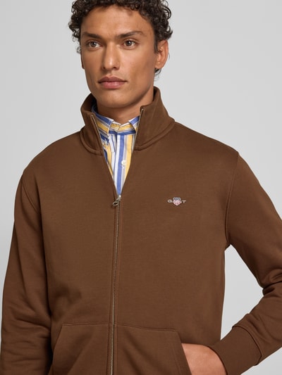 Männermodel trägt Sweatjacke mit Label-Stitching von Gant in Braun, Baumwoll-Mix, Regular Fit, Stehkragen, Reißverschluss, Nahaufnahme Oberkörper.