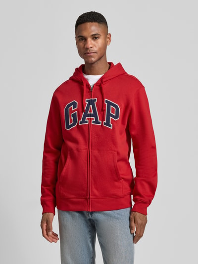 Männermodel trägt Sweatjacke mit Logo und Känguru-Tasche von GAP aus Baumwoll-Mix, Regular-Fit, rot, Reißverschluss, Ganzkörperansicht von vorne.