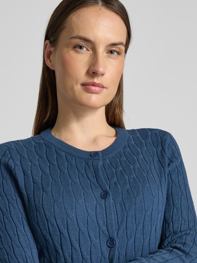 Frauenmodel trägt Regular Fit Strickjacke mit Viskose-Anteil Modell 'FANTASTIC' von Vero Moda in Uni-Blau, Zopfmuster, Nahaufnahme Oberkörper.