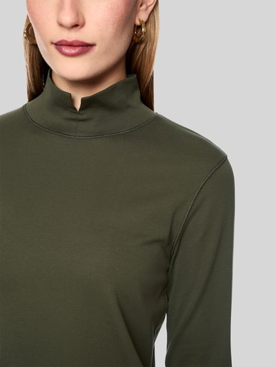 Frauenmodel trägt Longsleeve mit Stehkragen und Zierknöpfen von Marc Cain in Olivgrün, Baumwoll-Elasthan-Mix, Nahaufnahme Oberkörper. Slim Fit, glatte Textur, Rückenlänge bei Größe 36: 58 cm.