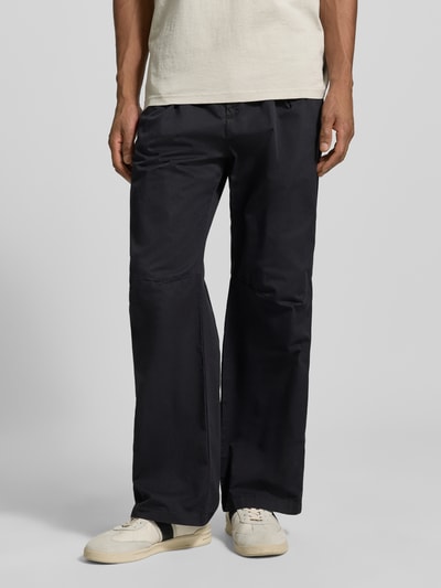 Męskimodel nosi Hose mit französischen Eingrifftaschen Modell 'Ethan' von Wood Wood z czarnej bawełny, luźny fason, wpuszczane kieszenie, szerokość w rozmiarze M: 42 cm, długość wewnętrzna nogawki: 75 cm. Ganzkörperansicht von vorne.