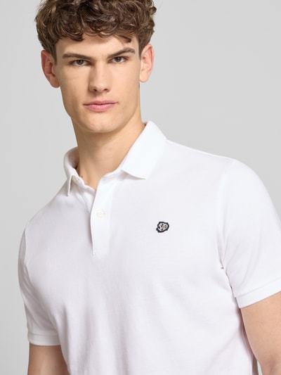Męski model nosi Regular Fit Poloshirt mit Logo-Stitching od Superdry z czystej bawełny, kołnierz polo, krótki rękaw, detal logo, krój regular fit, długość tyłu w rozmiarze M: 67 cm, jasnobiały kolor, tekstura gładka, zbliżenie na górną część ciała, widok z przodu.