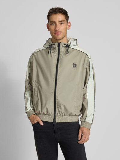 Männermodel trägt Regular Fit Jacke mit Kapuze Modell 'BAVO2621' von HUGO in Beige, Zweiwege-Reißverschluss, Logo-Detail, Ganzkörperansicht von vorne.