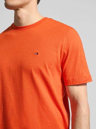 Mężczyzna nosi Regular Fit T-Shirt aus reiner Baumwolle von Tommy Hilfiger w jednolitym pomarańczowym kolorze, logo na piersi, jersey, krótki rękaw, okrągły dekolt, krój regular fit; zbliżenie na górną część ciała