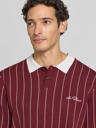 Männermodel trägt Regular Fit Poloshirt mit Logo-Stitching von Les Deux in Bordeaux mit weißen Streifen, reine Baumwolle, Nahaufnahme Oberkörper.