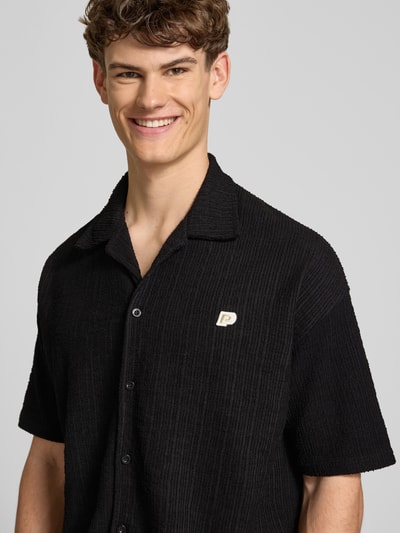 Männermodel trägt Regular Fit Freizeithemd mit Label-Patch Modell 'LIBCO' von Pegador, schwarzer Material-Mix, Knopfleiste, Nahaufnahme Oberkörper. Rückenlänge 72 cm, Schulterbreite 41 cm, Ärmellänge 35 cm bei Größe M.