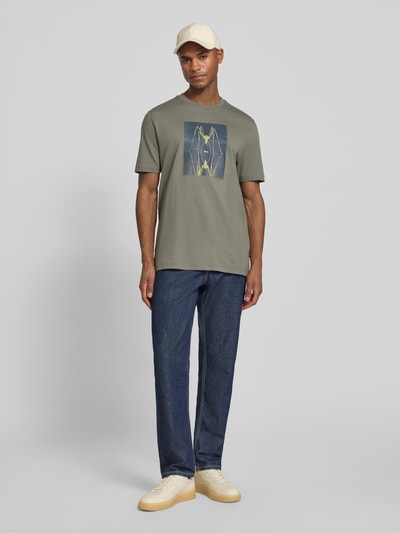 Männermodel trägt Regular Fit T-Shirt aus reiner Baumwolle Modell 'TE_CREATURE' von BOSS Orange in Oliv mit Motiv-Print, Ganzkörperansicht von vorne.